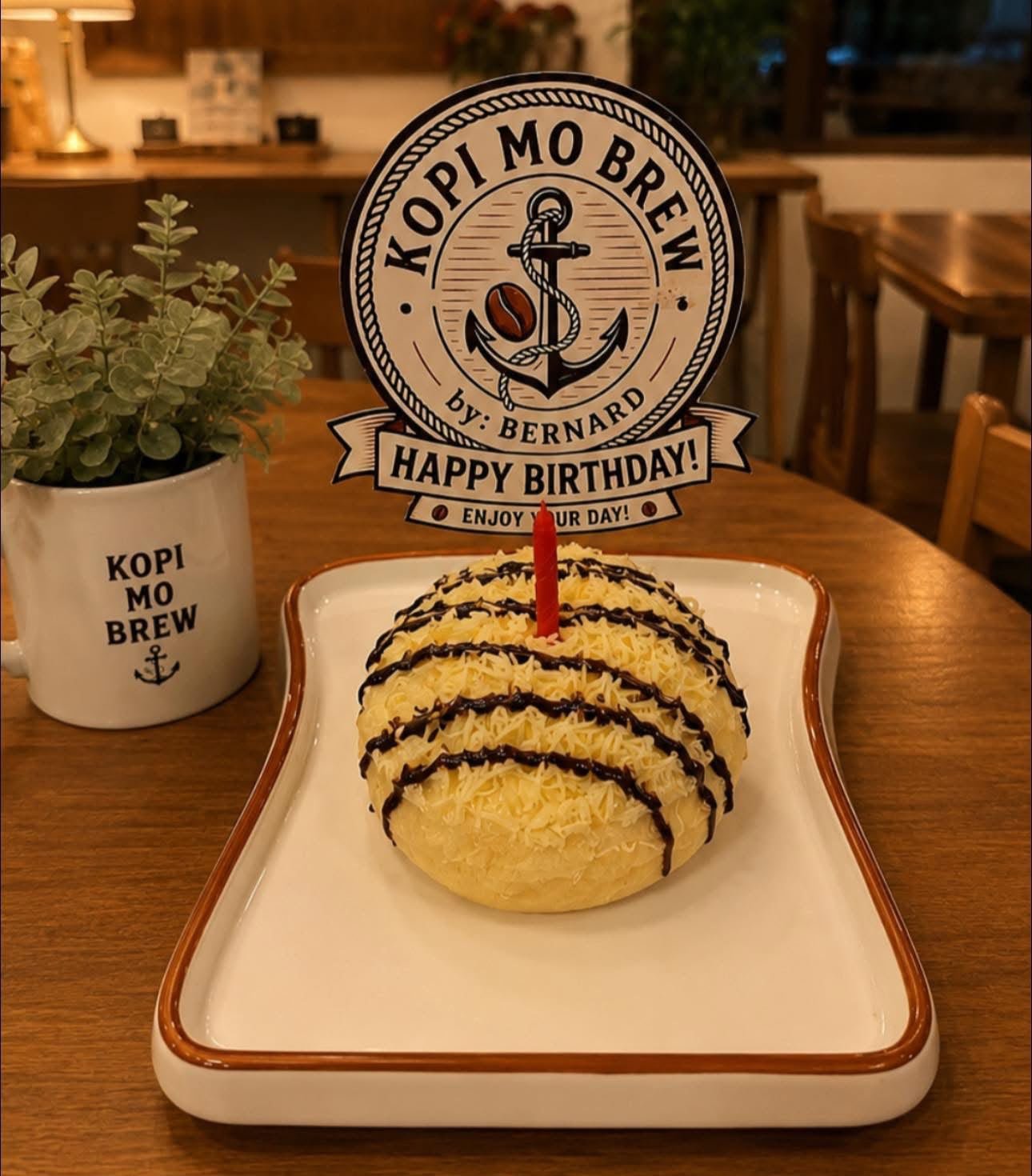 A cheese ensaymada with a single candle and a Kopi Mo Brew birthday topper